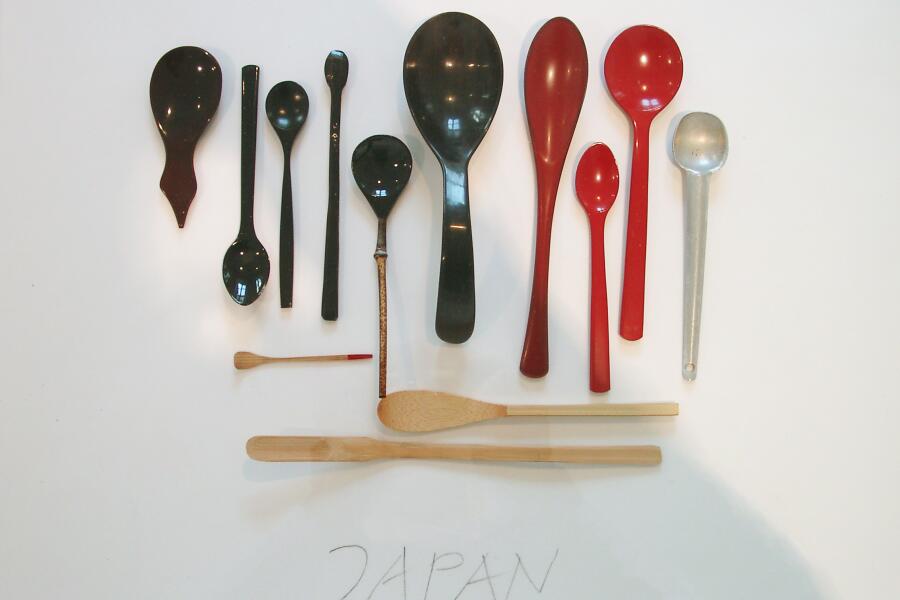 mehre Löffel in schwarzer und roter Farbe liegen in einer Tischvitrine. In einer großzügigen Handschrift steht das Wort Japan darunter.