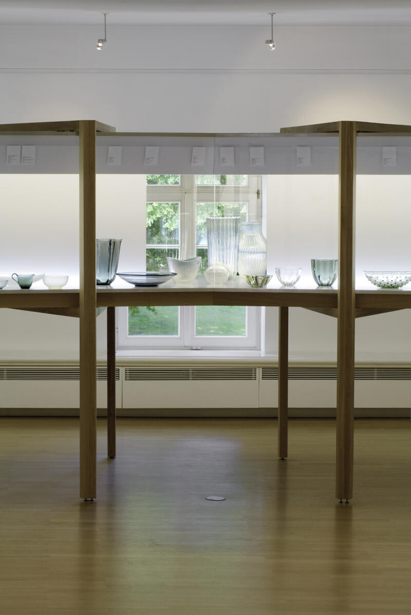  Vitrine mit filigranen Glas-Entwürfen von Wilhelm Wagenfeld. Im Hintergrund ein Fenster des Ausstellungsraumes.